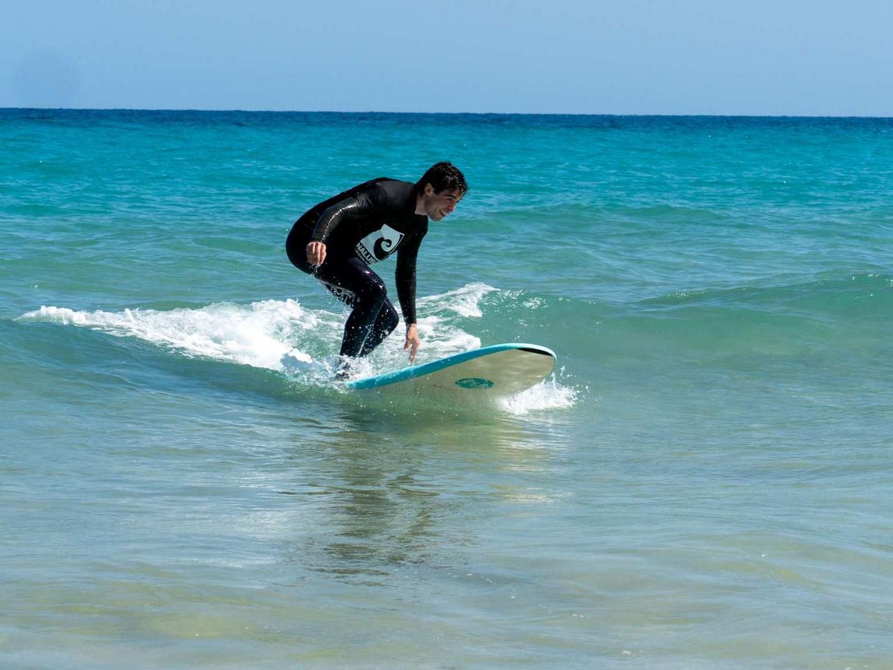 Alex steht auf dem Surfbrett und surft im türkisblauen Wasser am TYPO3 Surfcamp