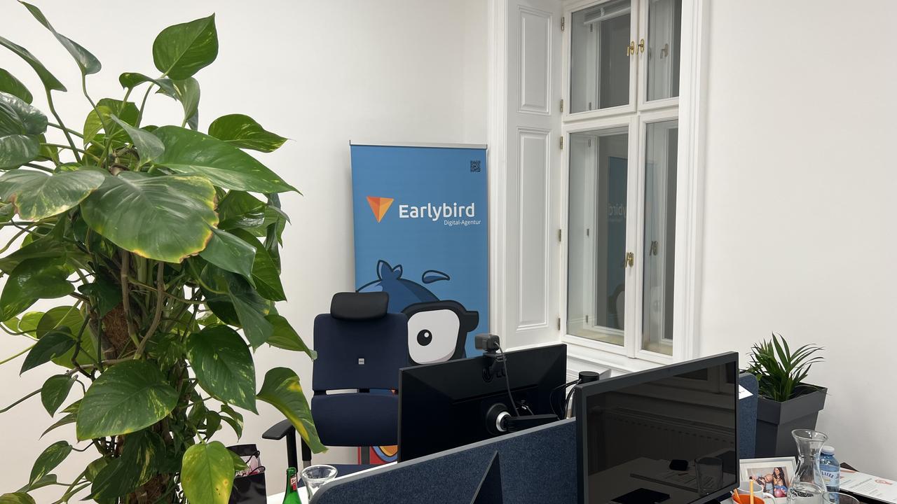 Arbeitsplatz im Earlybird Büro mit Werbebanner im Hintergrund.