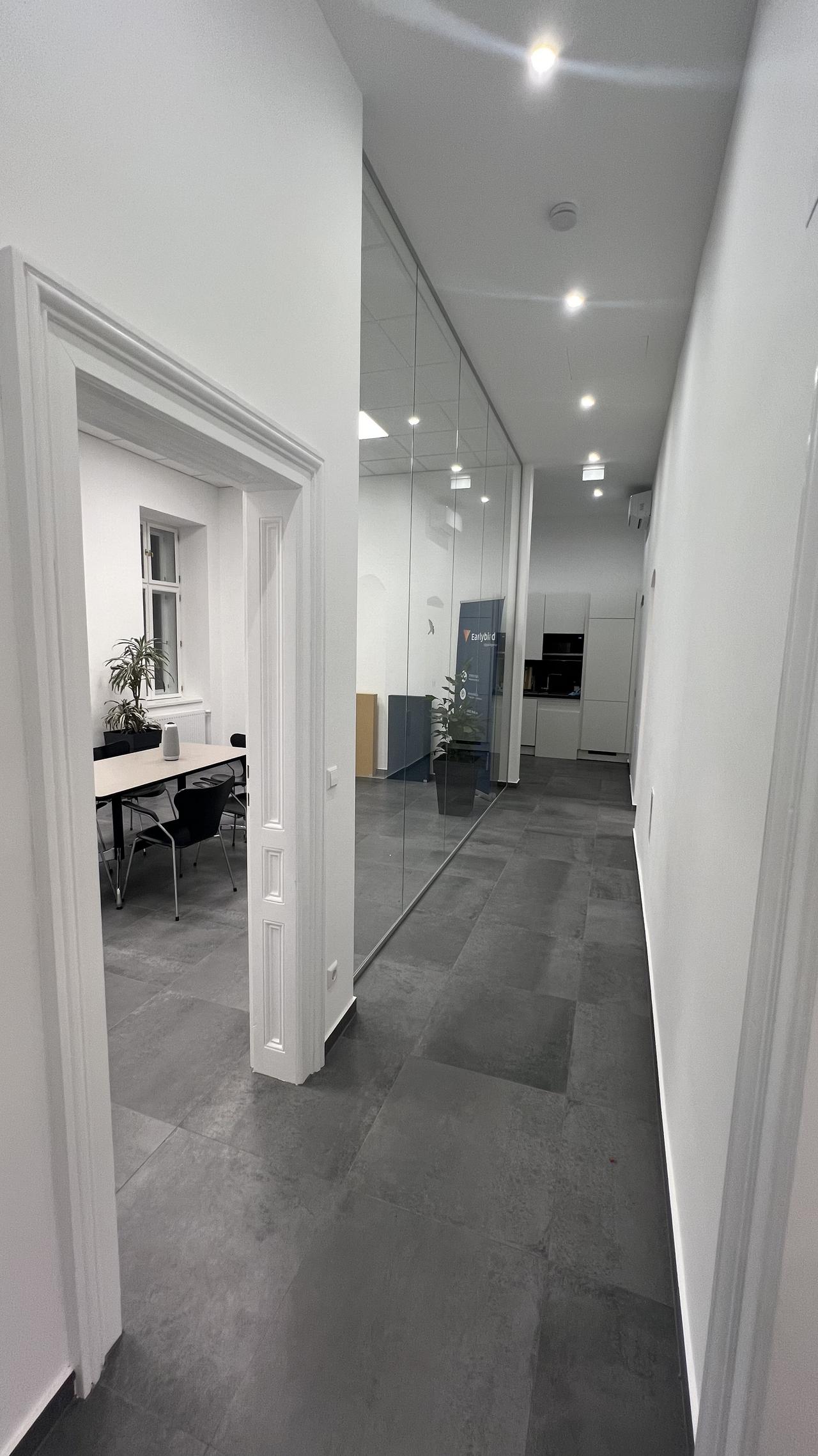Blick vom Eingang des Earlybird Office in den Gang mit hohen Räumen, grauem Schieferboden und Glaswand.